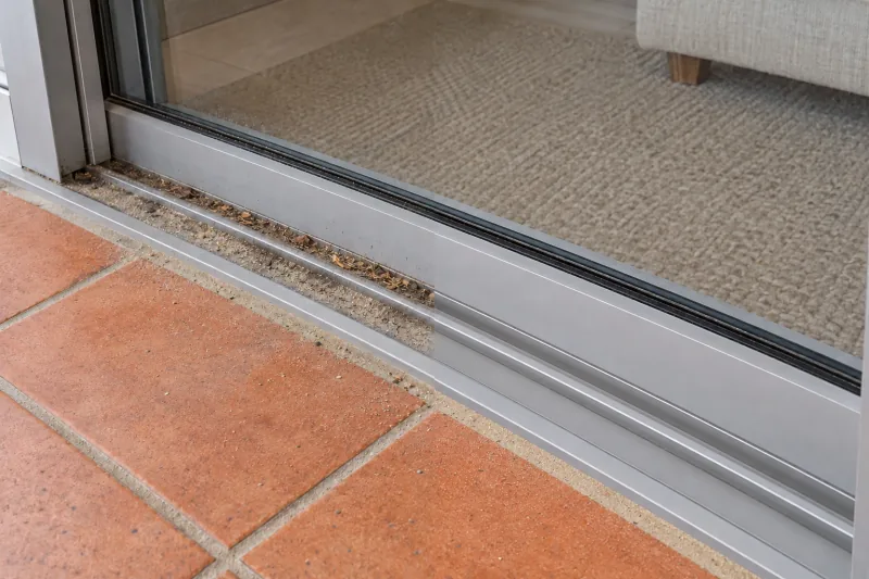 Dirt packed in a sliding door track over tiles, the right half cleaned – deep cleaning in North Canberra