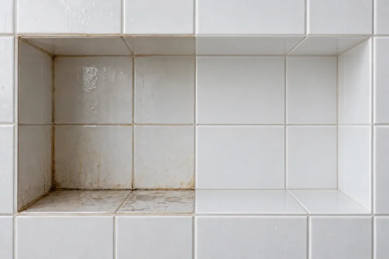 Tiled shower niche with soap scum and stains, the right half cleaned – end of lease cleaning in Canberra