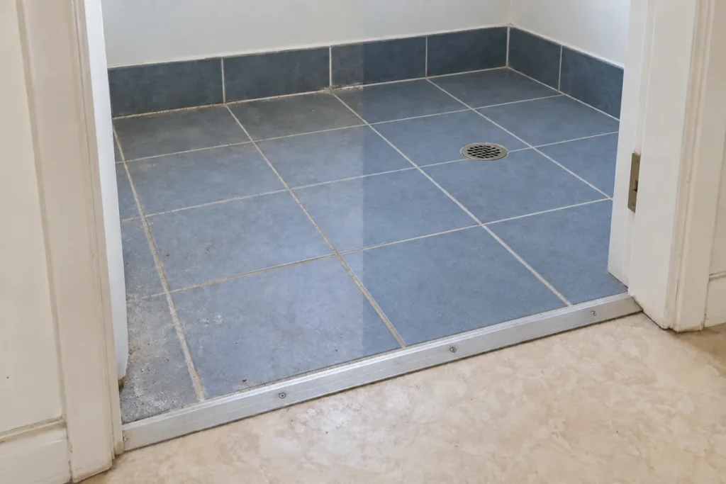 Blue laundry floor tiles with dust at the threshold, the right half cleaned – end of lease cleaning in Deer Park