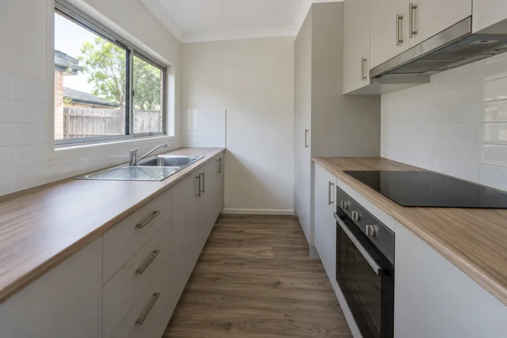 Empty galley kitchen with white cabinets, timber benchtops and wall oven – end of lease cleaning in Fitzroy