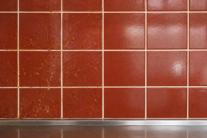Red tiled splashback spotted with grease, the right half cleaned to a shine – end of lease cleaning in North Melbourne