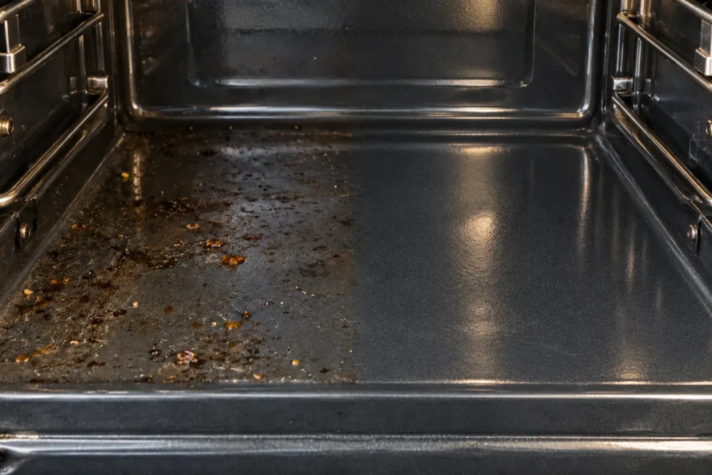 Oven floor with burnt food spatter on the left, the right half cleaned – oven cleaning in South Canberra